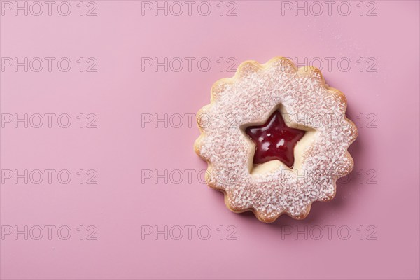 Top view of single traditional Linzer cookie with red fruit jam on pink background with copy space.