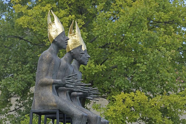 Sculpture Enthroned by Volkmar Kühn 2021, three bishops with golden mitres sitting on stool, row,