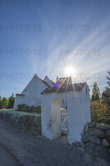 Whitewashed church in Dalby, backlight, stone wall made of boulders, entrance gate, Fyn, North