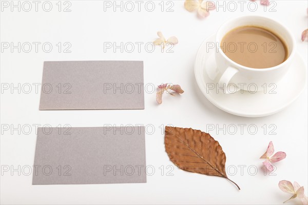 Composition with gray paper business card, brown beech autumn leaves, hydrangea flowers and cup of