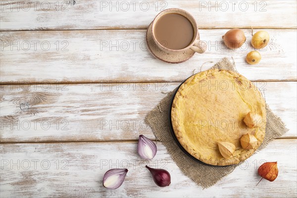 Autumn onion pie and cup of coffee on white wooden background and linen textile. Top view, flat