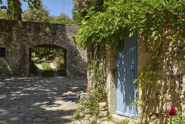 Blue entrance door of a house and wall with passageway in La Roque-sur-Cèze, Département Gard,