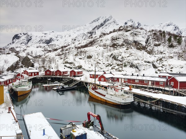 Red wooden houses in the harbour of the authentic fishing village of Nusfjord, snow-capped