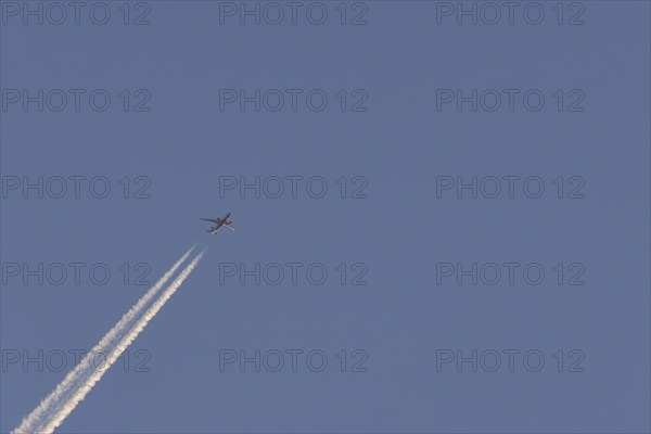 Boeing 787-8 Dreamliner aircraft flying across a blue sky with a vapour trail or contrail behind,