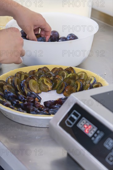 Person arranges plum halves on the pastry base of a cake
