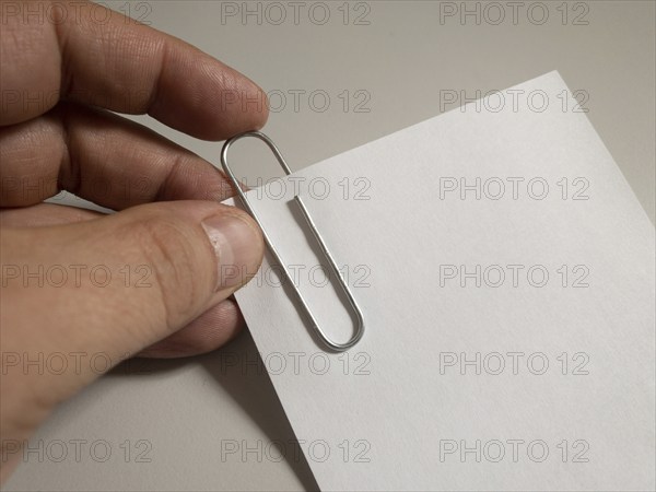 A hand attaches a paper clip to a piece of white paper