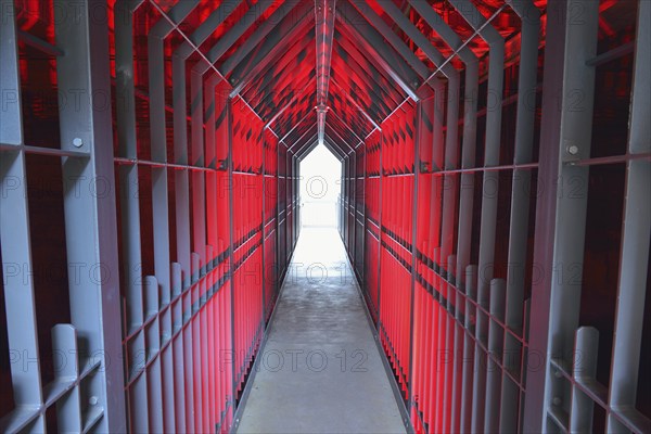A long tunnel with red lighting and metallic structures conveys a futuristic and industrial