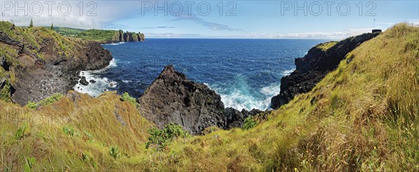 Panorama of a rocky coastal view with rugged cliffs plunging into the blue sea under a clear sky,