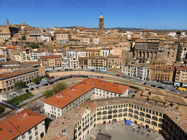 Aerial view of a historic city with many tiled roofs and a striking tower in the centre, aerial