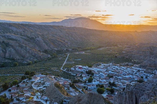 A village lies in a valley surrounded by hills and mountains as the sun sets and the valley glows