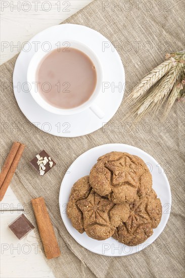 Homemade oatmeal cookies with a cup of cocoa on a linen textile and white wooden background. top