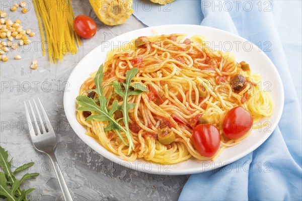 Corn noodles with tomato sauce and arugula on a gray concrete background and blue textile. Side