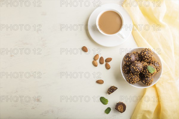 Chocolate caramel ball candies with almonds and a cup of coffee on a white wooden background and