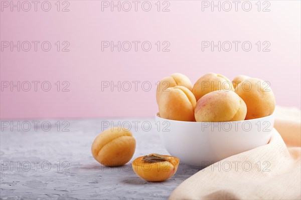 Fresh orange apricots in white bowl on gray and pink pastel background. side view, copy space,