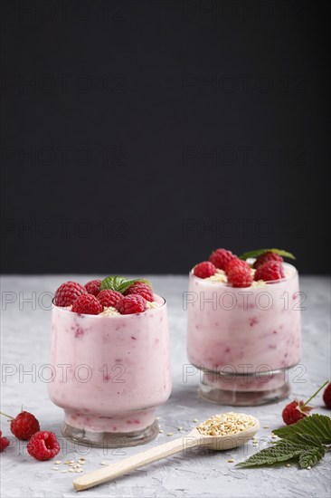 Yoghurt with raspberry and sesame in a glass and wooden spoon on gray and black background. side