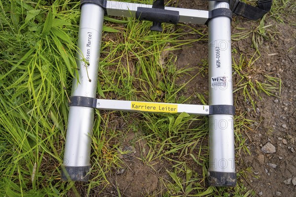 A metal ladder lies on a grass- and dirt-covered ground surface, fibreglass installation, Calw