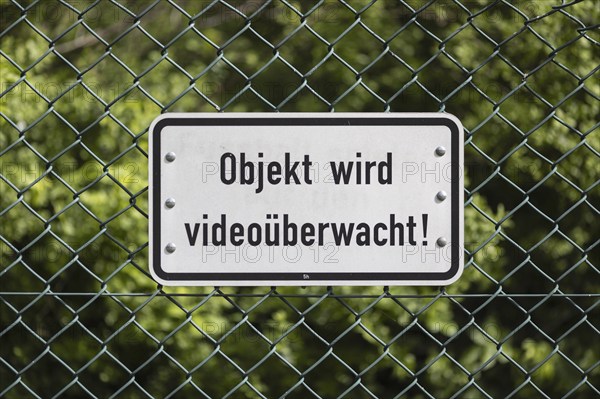 Sign mounted on a green wire mesh fence with the inscription: Objekt wird videoüberwacht! in