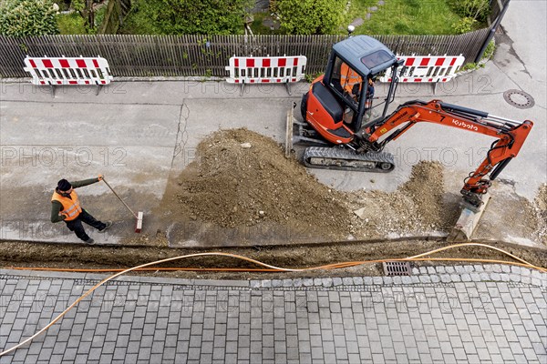 Construction workers lay fibre optic cable in trench under asphalt, cable trench, excavator,