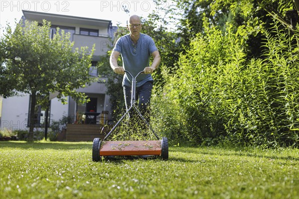 Man with hand lawnmower in the garden, Bonn, 04.07.2024