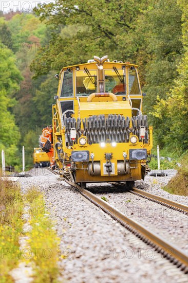 Yellow tractor moving on a railway track through a densely wooded area, Hermann Hesse Bahn track