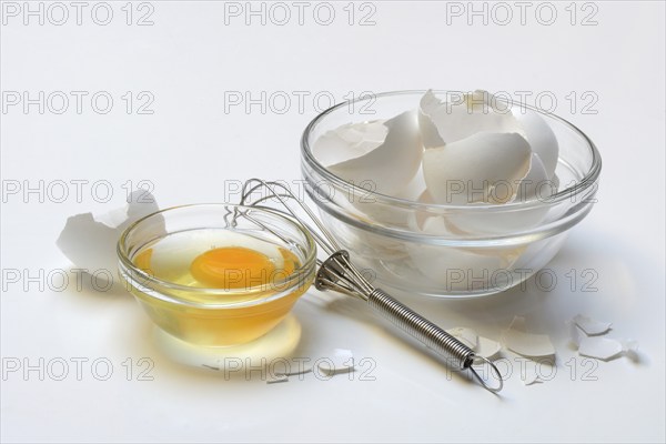 Egg whites and egg yolks in glass bowl and egg shells, whisk