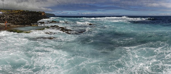 Stormy waves crash against a rocky shore under a cloudy sky, seawater bathing establishment,