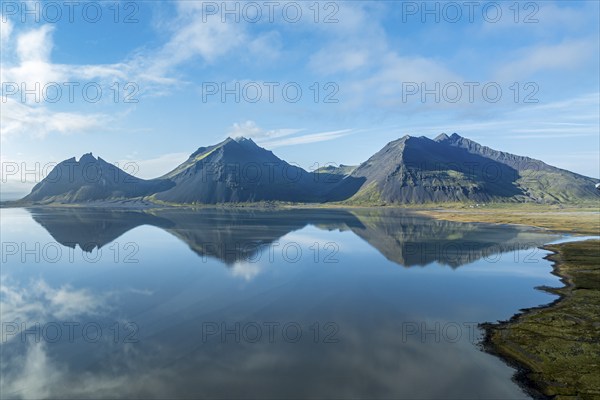 Aerial view over the calm sea to Mt. Brunnhorn and Vestrahorn, east of Höfn, clouds are reflected