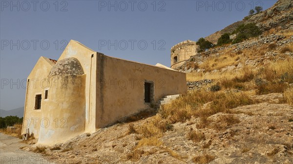A historic building on a hillside with dry vegetation and mountains in the background, Venetian Sea
