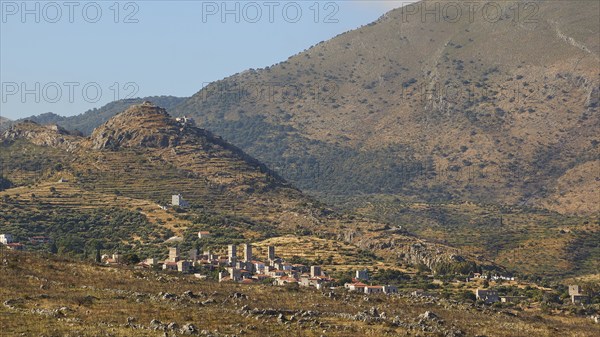 View of a quiet rural village surrounded by mountainous landscape under a clear blue sky,