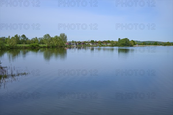 Quiet lake with trees on the shore, in the background a campsite, leisure area, under blue sky,