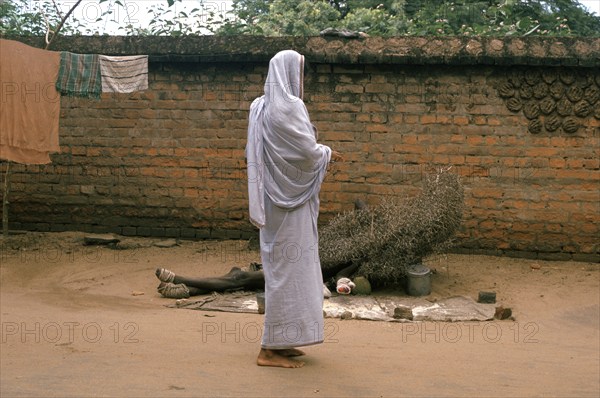 A hindu widow is giving alms to a leper (Puri, India) . The man is lying on the ground under a pile