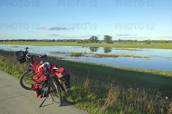 A bicycle stands at the edge of a dyke path next to a flooded Elbe meadow in a wide meadow