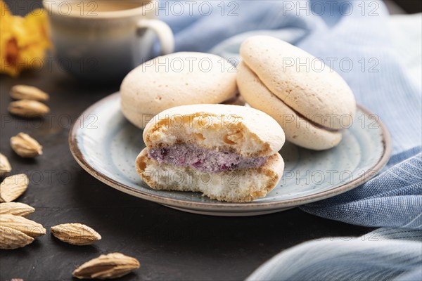 Meringues cakes with cup of coffee on a black concrete background and blue linen textile. Side