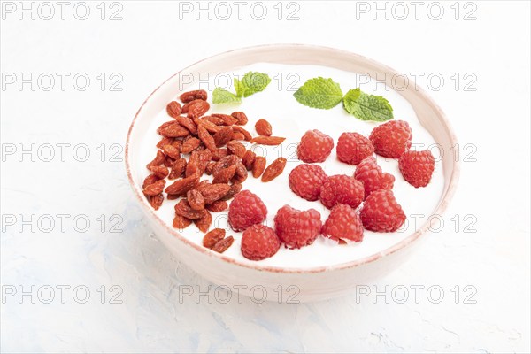 Yogurt with raspberry and goji berries in ceramic bowl on white concrete background. Side view,