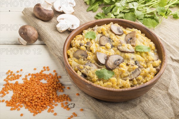 Lentils porridge with champignons and coriander in a wooden bowl on a white wooden background and