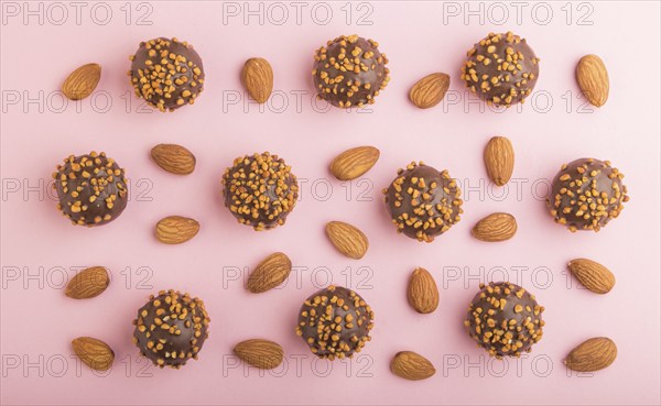 Chocolate caramel ball candies with almonds in a row on a pastel pink background. top view, flat