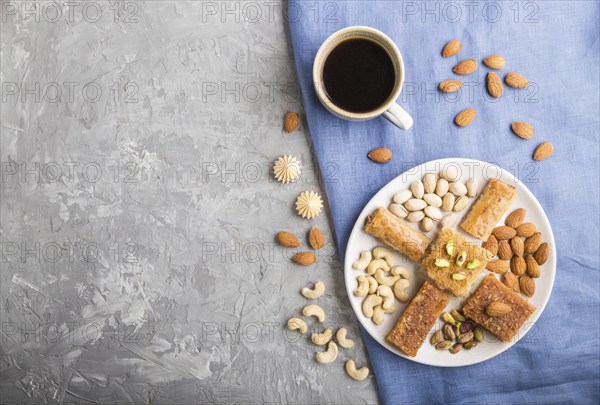 Traditional arabic sweets (basbus, kunafa, baklava), a cup of coffee and nuts on a gray concrete