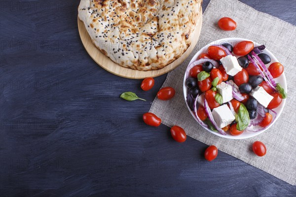 Greek salad with fresh cherry tomatoes, feta cheese, black olives, basil and onion on black wooden