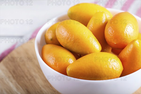 Kumquats in a white plate on a white wooden background, close up