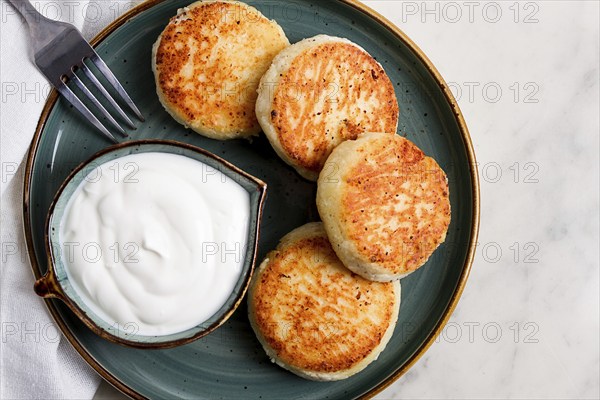 Fried, Cottage cheese pancakes, with sour cream, Cheesecakes, on a marble table, top view, no