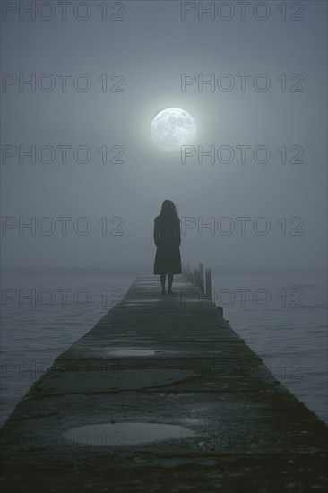 Silhouette of a lonely, sad woman on a concrete footbridge on a foggy full moon night, symbolic