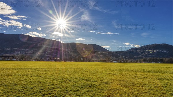 Bright sun over a green meadow in front of a mountain range in a clear sky, Bad Feilnbach