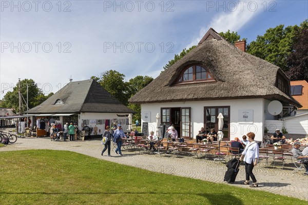 Lively café with people sitting outside, surrounded by thatched-roof houses, Rügen, Hiddensee