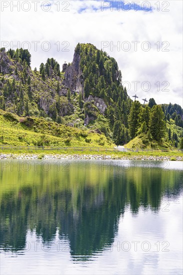 A clear mountain lake reflects the surrounding trees and mountains under a cloudy sky, Penken,