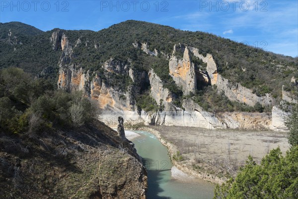 A river flows through a rocky landscape surrounded by high, steep cliffs and wooded mountains under