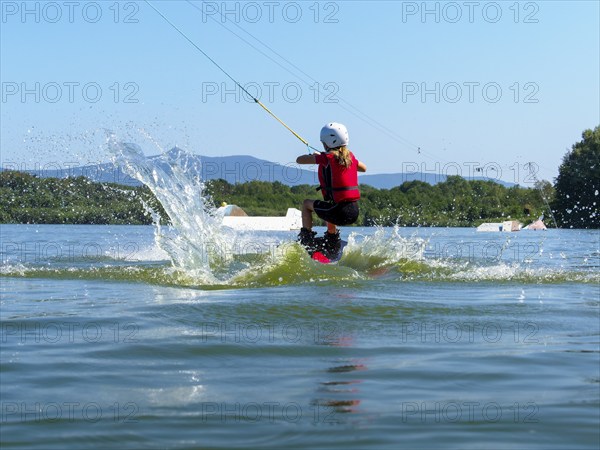 Boy or girl, jump over jump with wakeboard, red life jacket and water sports, water skiing in