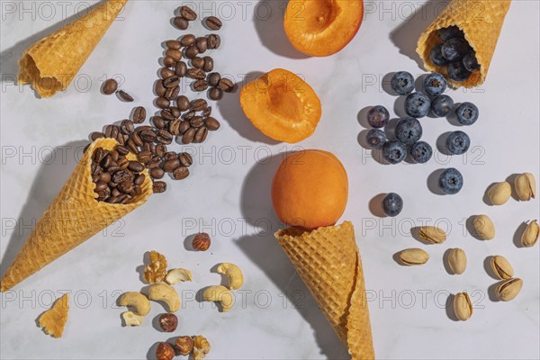 Ice cream cones with coffee beans, apricots, blueberries, pistachios and nuts on a marble