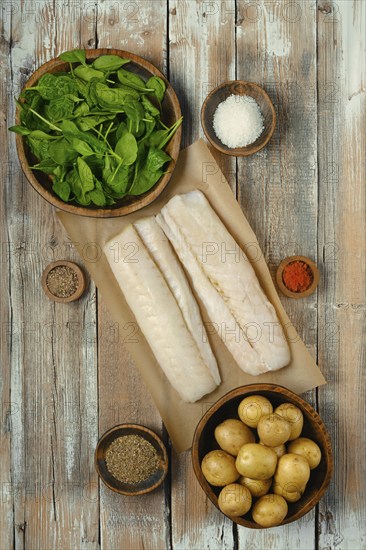 Fresh fish fillets on parchment paper surrounded by bowls of spinach, potatoes, and various spices,