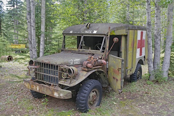 Rusty, old army ambulance, with Red Cross symbol between trees in the forest, former army camp,