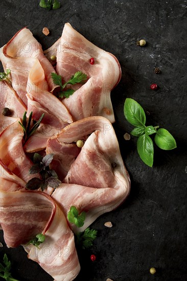 Raw bacon, sliced, with micro greenery and spices, on a black background, close-up